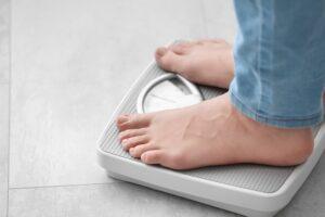 A person in jeans stands on a scale trying to understand the reasons why they’re not losing weight on tirzepatide.